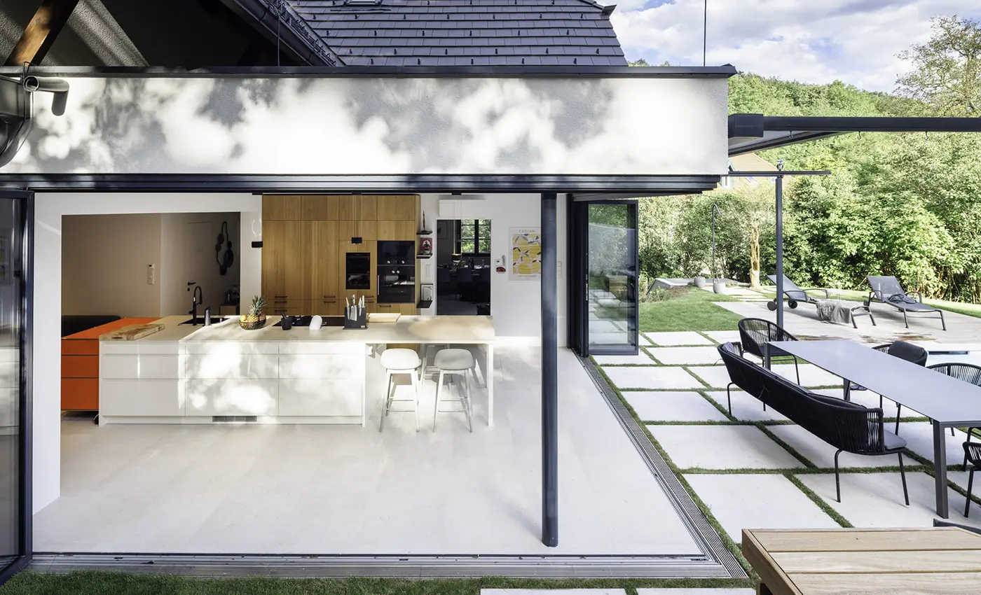 Zwei Glas-Faltwände einer modernen Küche sind komplett zur Terrasse hin geöffnet.