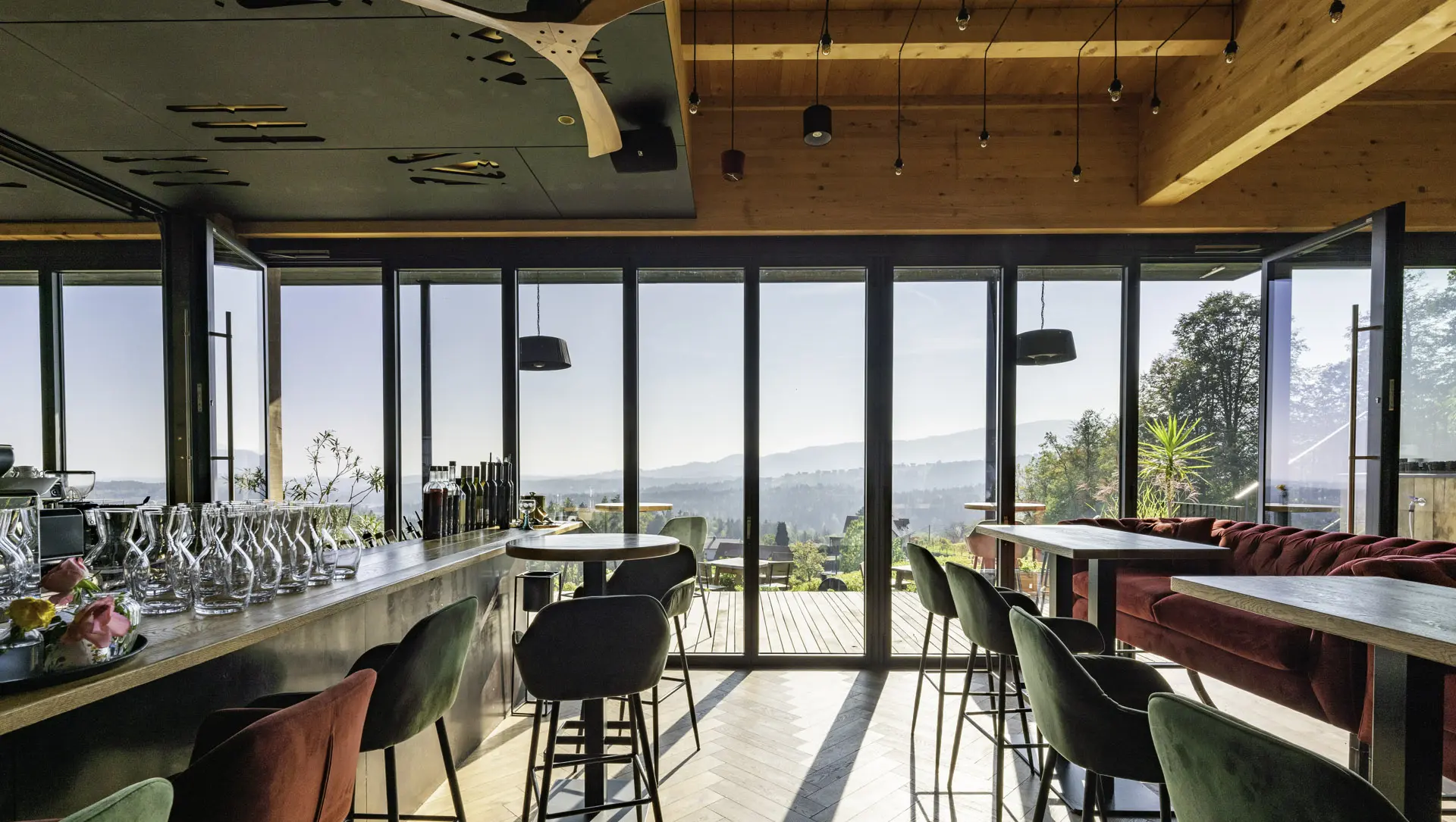 Modern und gemütlich eingerichtetes Lokal mit Ausblick durch eine Glas-Faltwand-Front auf ein grünes Landschaftspanorama.