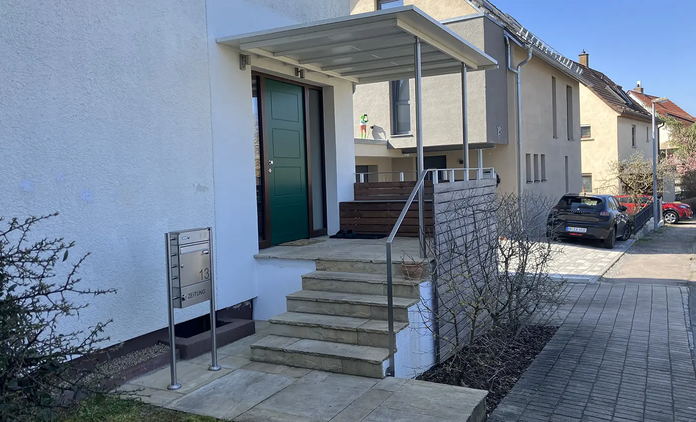 Grüne Haustür mit braunem Holzrahmen und Fensterglas links und rechts daneben