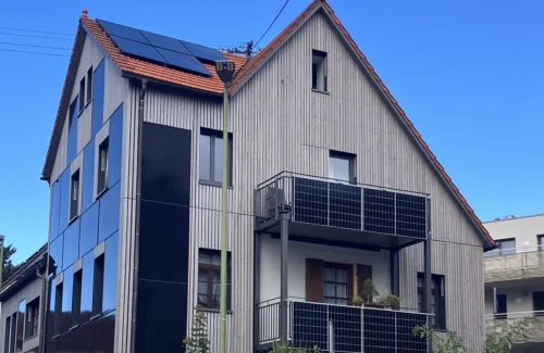 Haus mit Holzfassade und zahlreichen Photovoltaik-Paneelen auf dem Dach, der Fassade und dem Balkon.