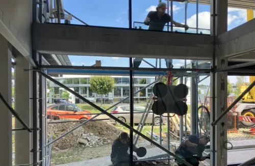 Arbeiter, die gerade zu dritt ein Glasfenster in eine Metallkonstruktion einsetzen