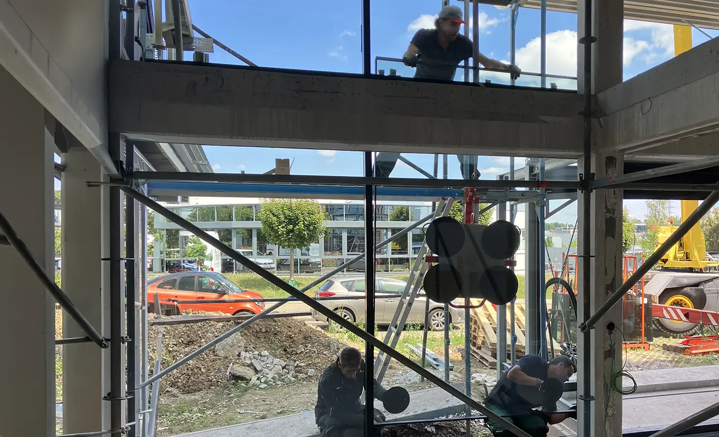 Arbeiter, die gerade zu dritt ein Glasfenster in eine Metallkonstruktion einsetzen